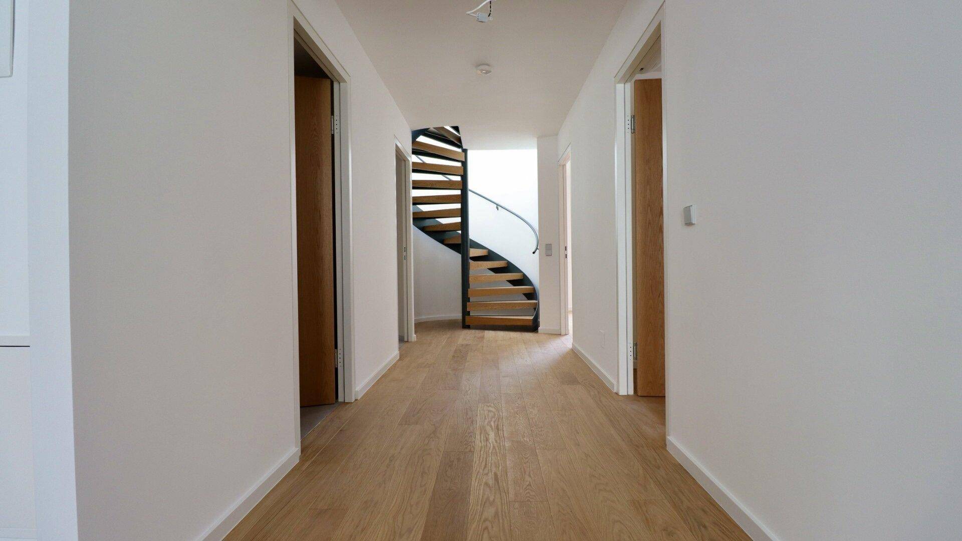 Langer Flur mit Holzboden und Blick auf eine elegante Wendeltreppe, die die Etagen verbindet.