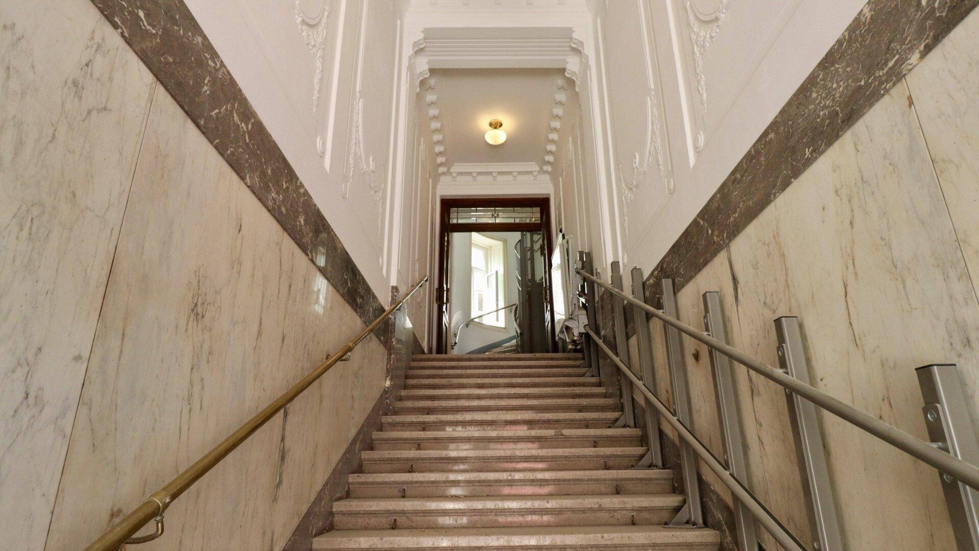 Elegantes Treppenhaus mit Marmorverkleidung, Stuckdecken und klassischem Geländer in einem Altbau.