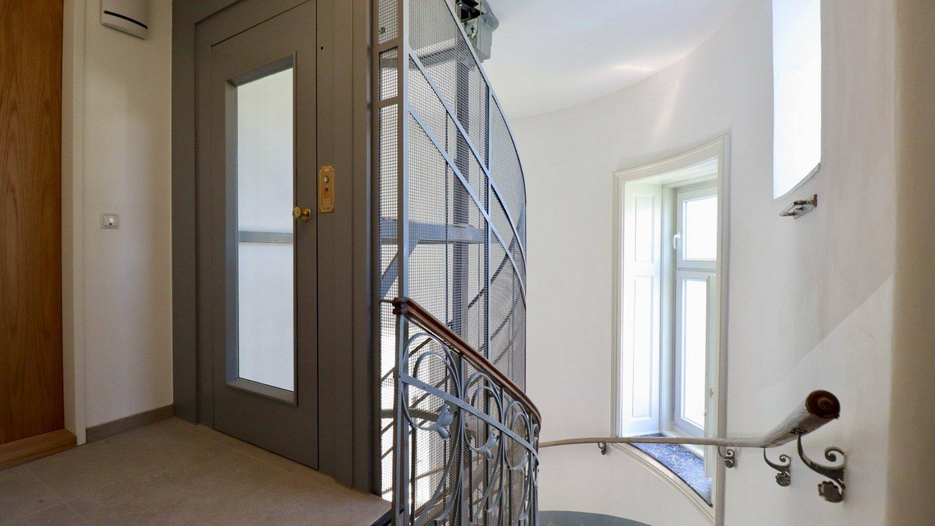 Stilvolles Treppenhaus mit modernem Aufzug und geschwungenem Geländer in einem gepflegten Gebäude.