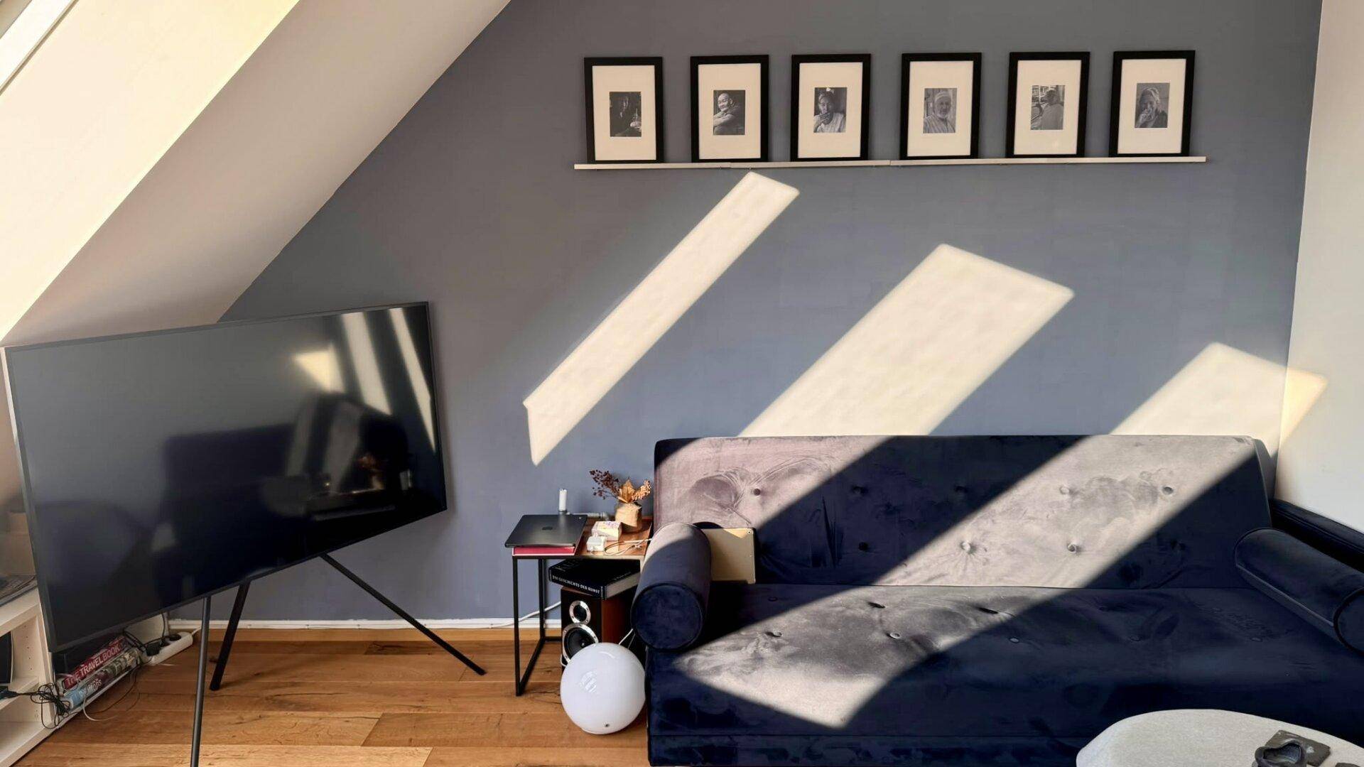 Helles Wohnzimmer mit schräger Decke, Holzboden und modernem Fernseher, durchflutet von Sonnenlicht.