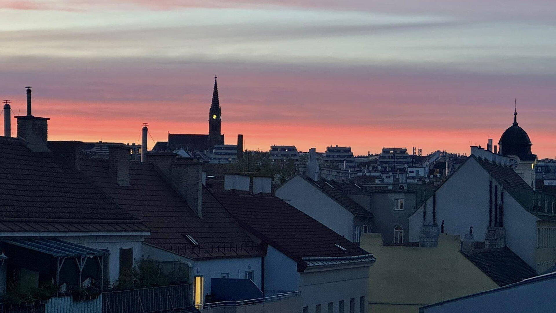 Panoramablick über die Stadt bei Sonnenuntergang mit leuchtendem Himmel und Kirchturm in der Ferne.