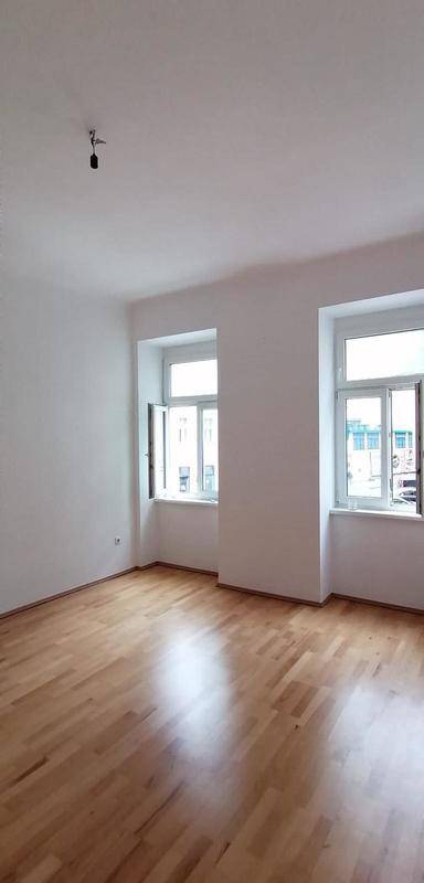 Geräumiges Wohnzimmer mit Parkettboden und großen Fenstern, die viel Tageslicht hereinlassen.