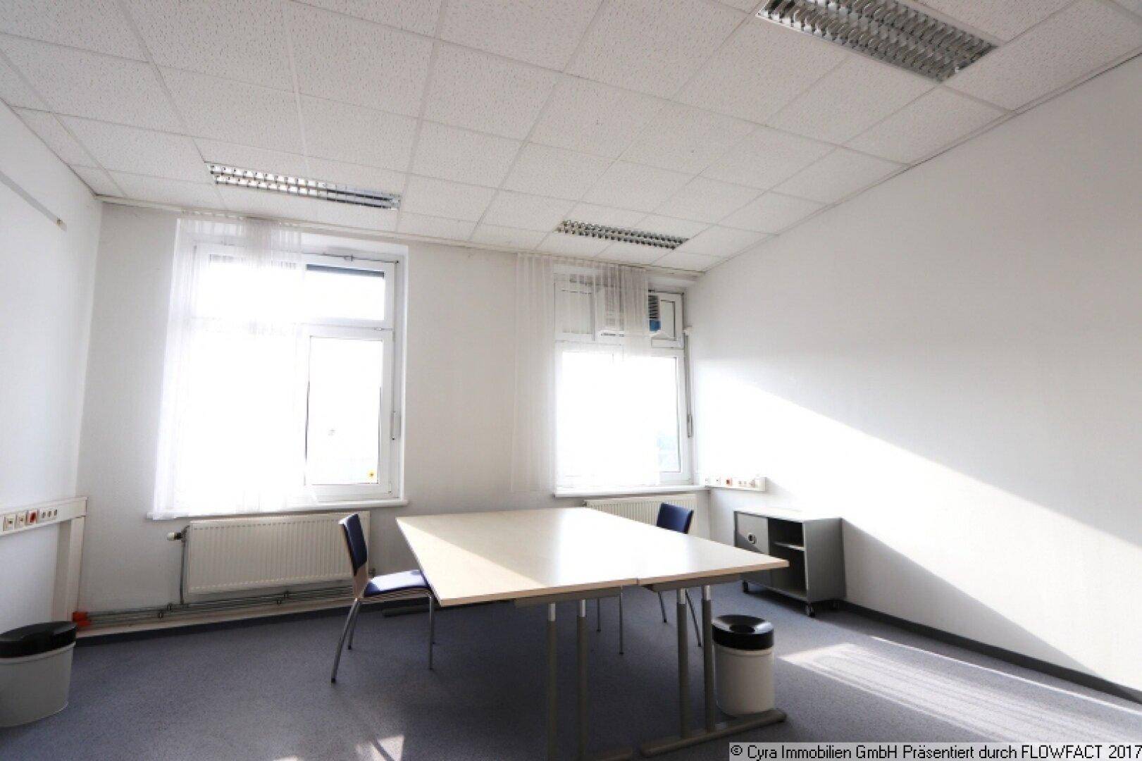 Helles Büro mit zwei großen Fenstern, einem Besprechungstisch und Stühlen, ideal für kleine Teams.
