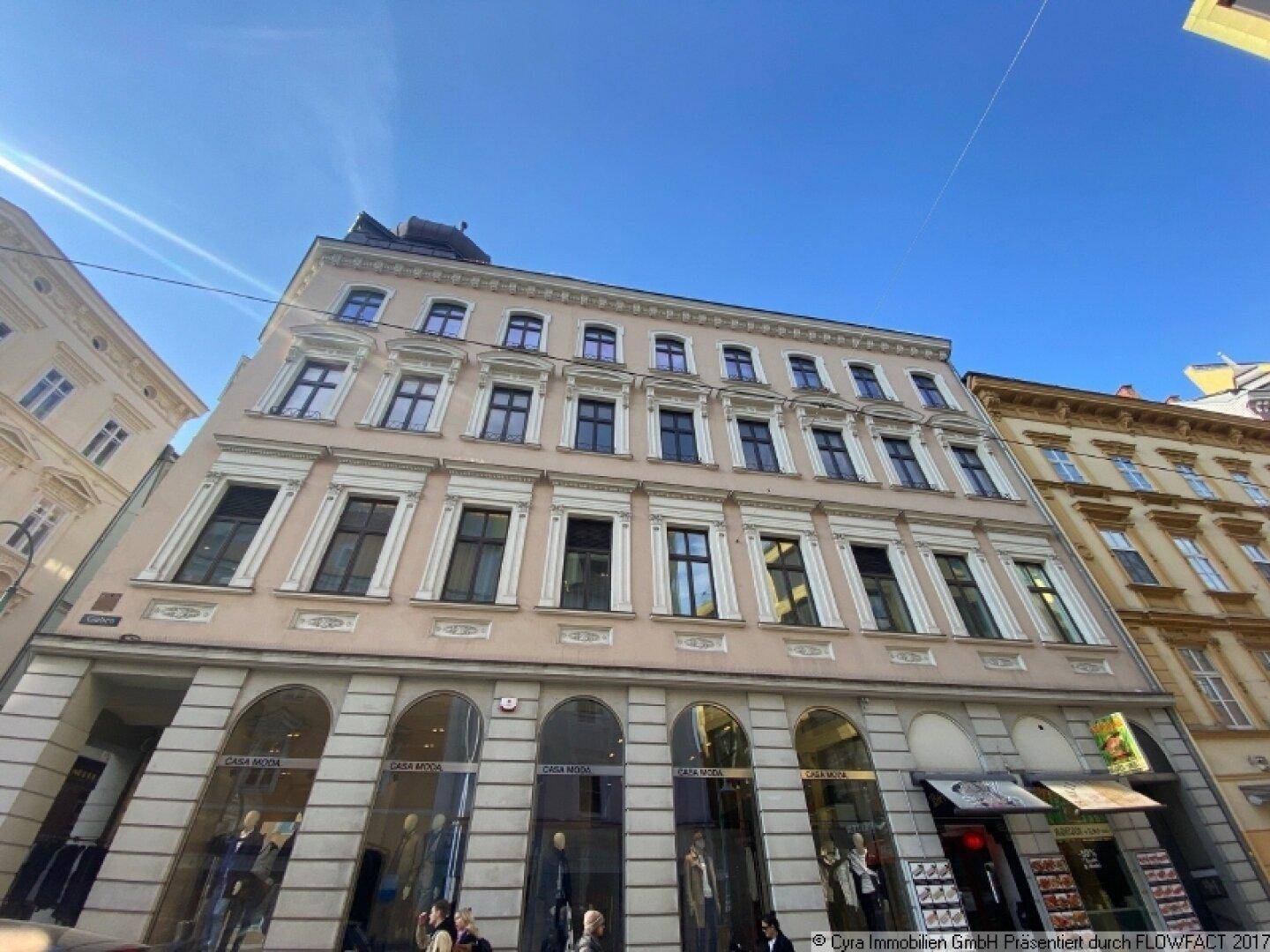 Detailansicht der historischen Fassade eines Gebäudes mit großen Fenstern und Geschäften im Erdgeschoss.