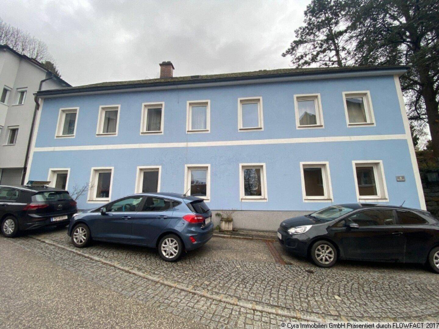 Altes Wohnhaus mit blauer Fassade und vielen Fenstern an einer Kopfsteinpflasterstraße.