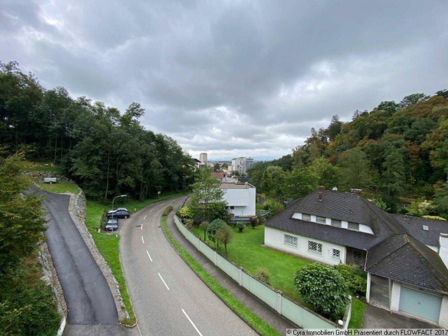 Weitblick über die umliegende Wohngegend mit Häusern, Straßen und bewaldeten Hügeln unter bewölktem Himmel.