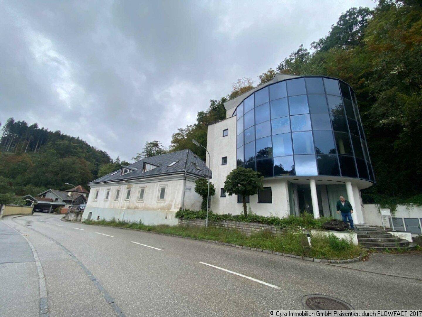 Ansicht des Gebäudes von der Straße, mit markanter Glasfassade des modernen Teils und dem angrenzenden Altbau.