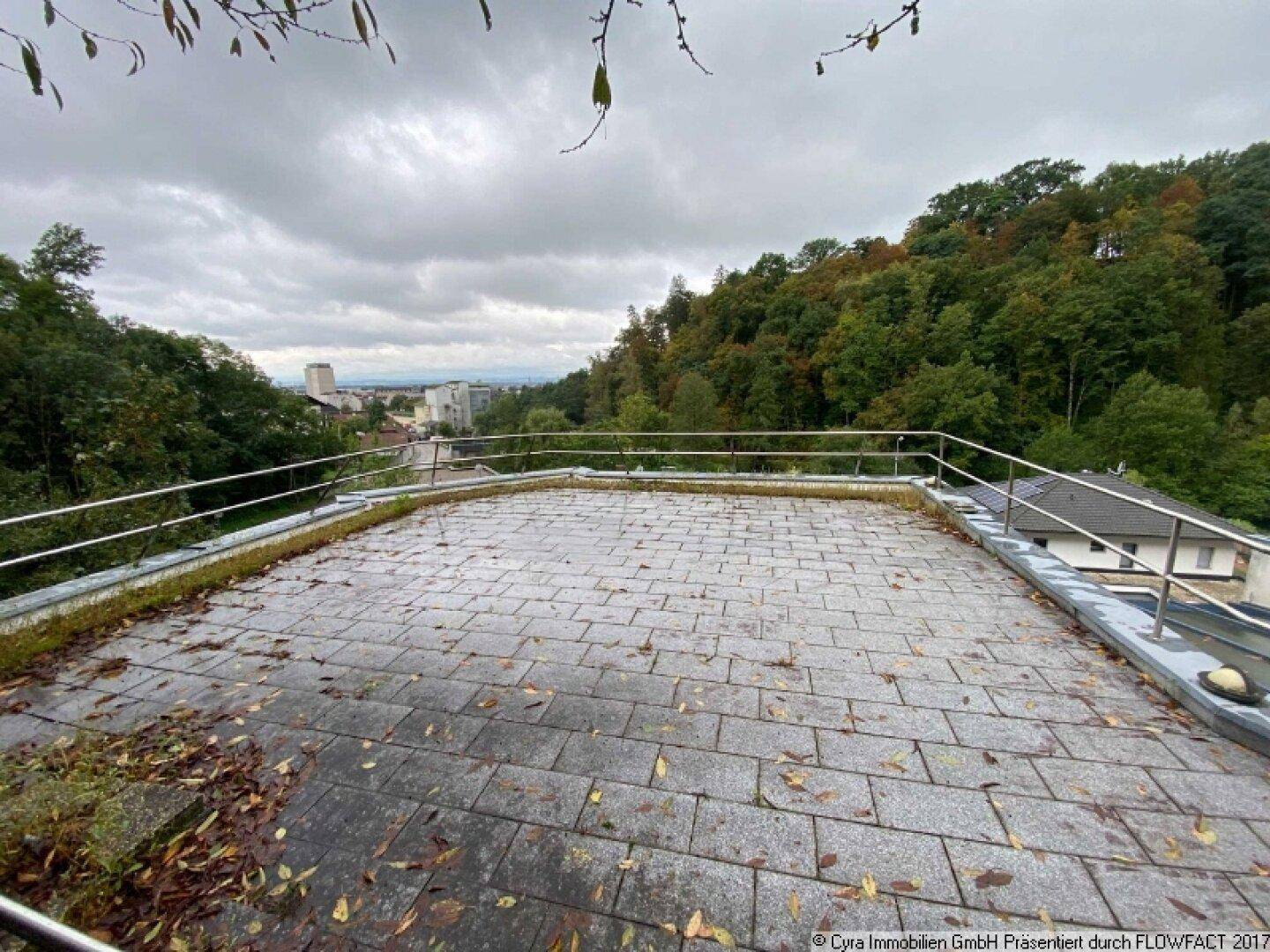 Geräumige Dachterrasse mit Steinplatten und Metallgeländer, bietet einen weiten Blick auf die Umgebung.