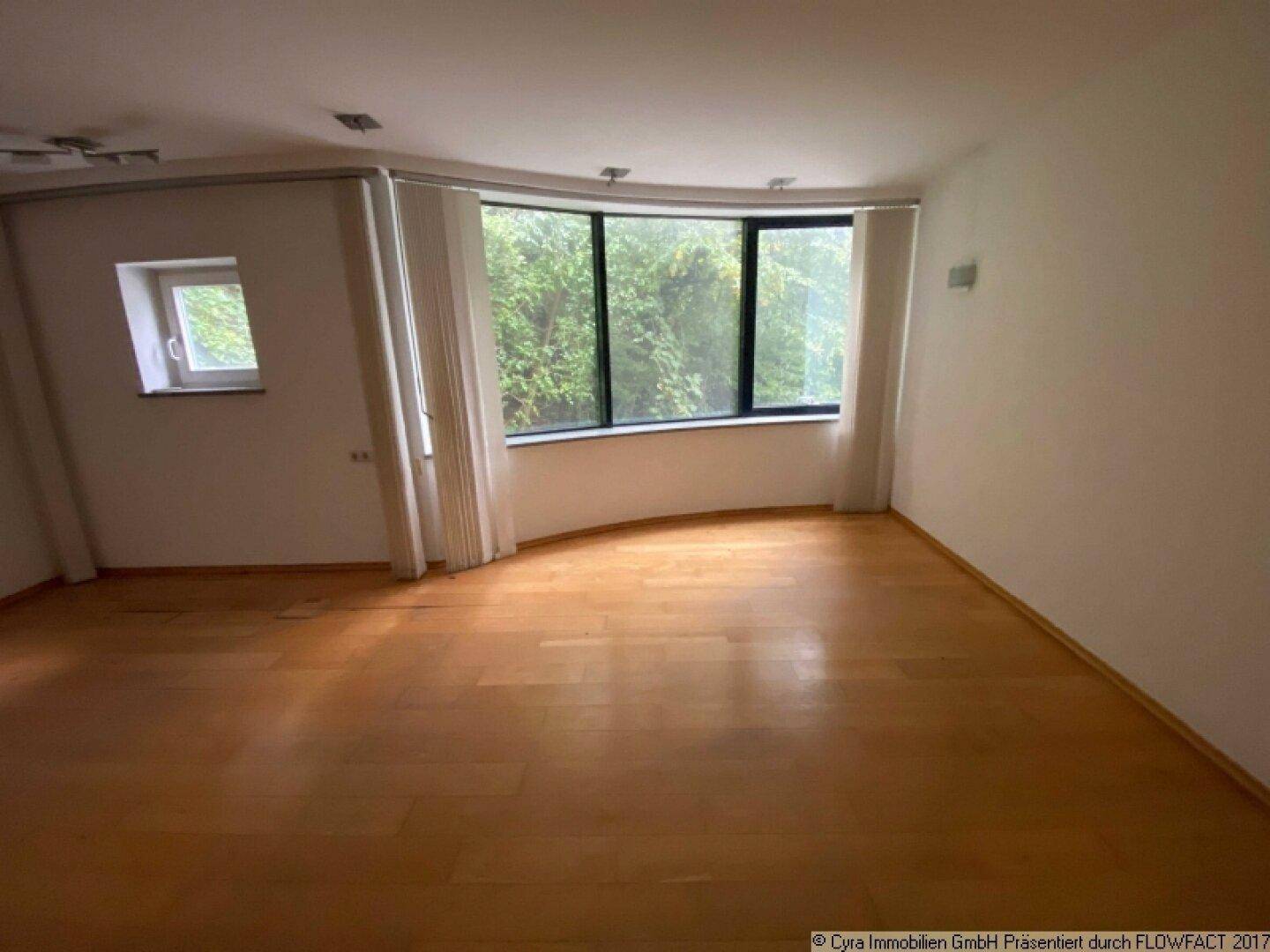 Heller Raum mit Parkettboden und einer großen, gebogenen Fensterfront, die viel Tageslicht hereinlässt.