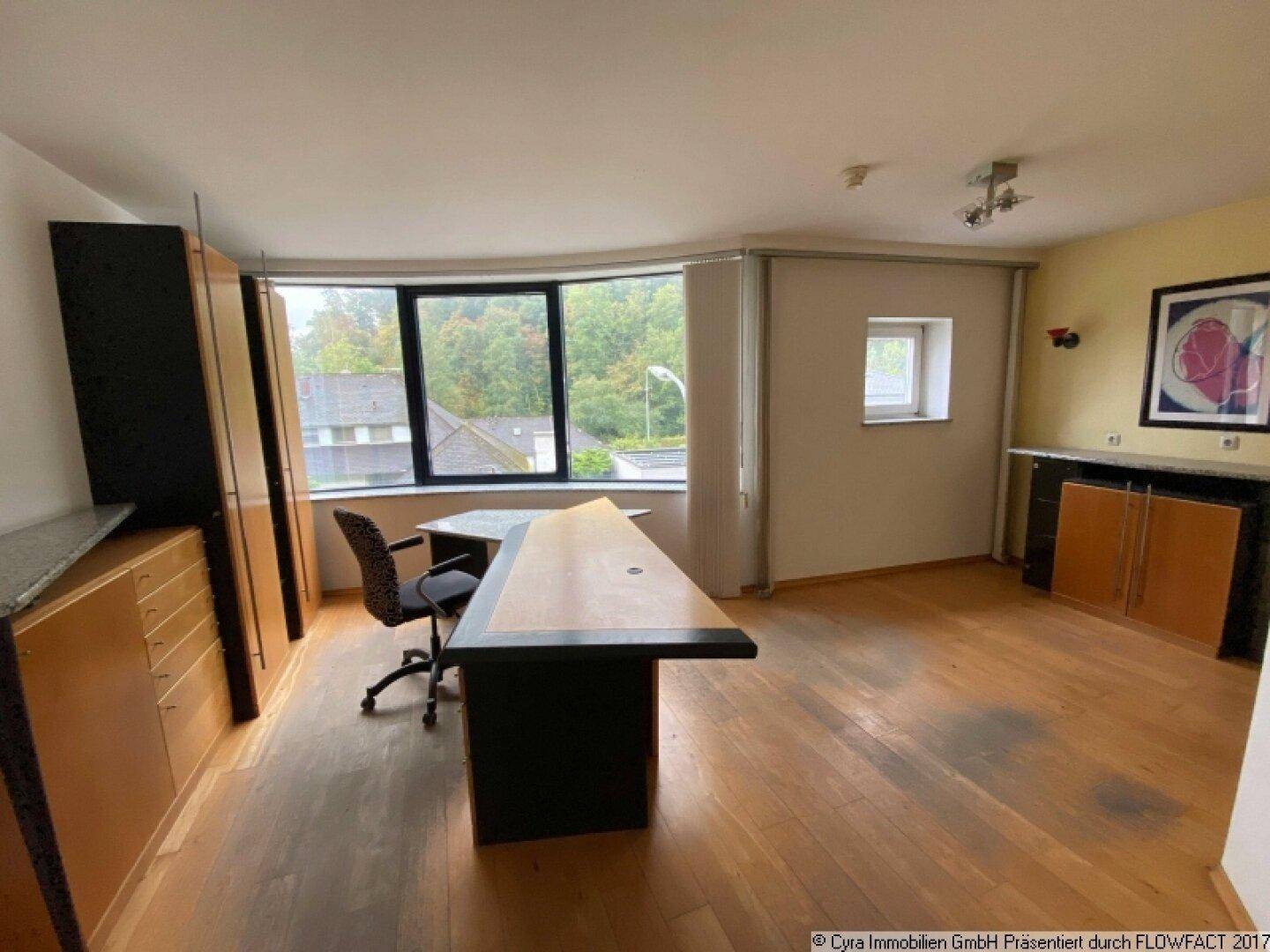 Geräumiges Büro mit Schreibtisch, Einbauschränken und großen Fenstern, die den Raum hell erscheinen lassen.