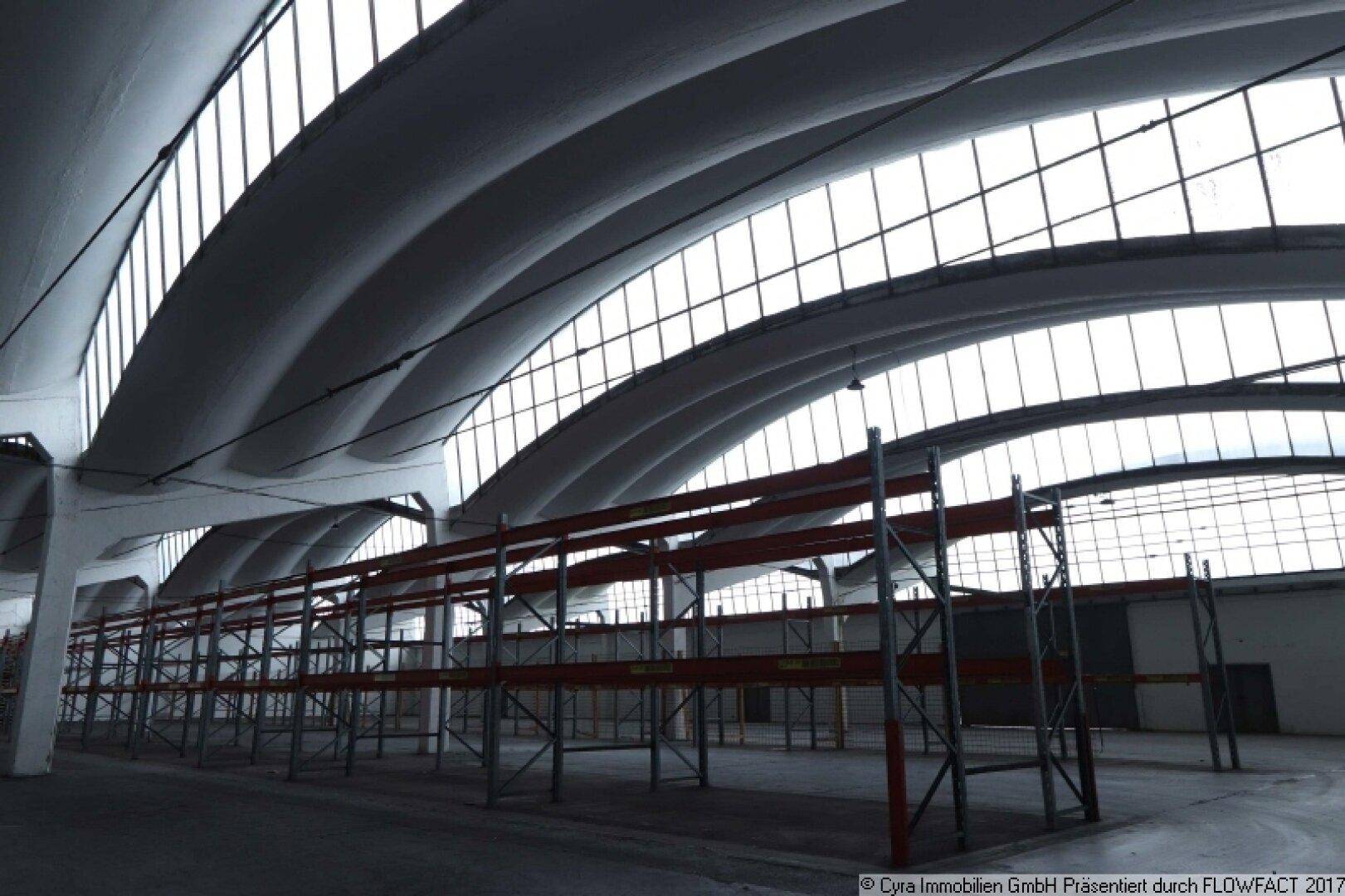 Geräumige, leere Lagerhalle mit beeindruckenden gewölbten Decken und großen Fensterfronten, die viel Tageslicht hereinlassen.