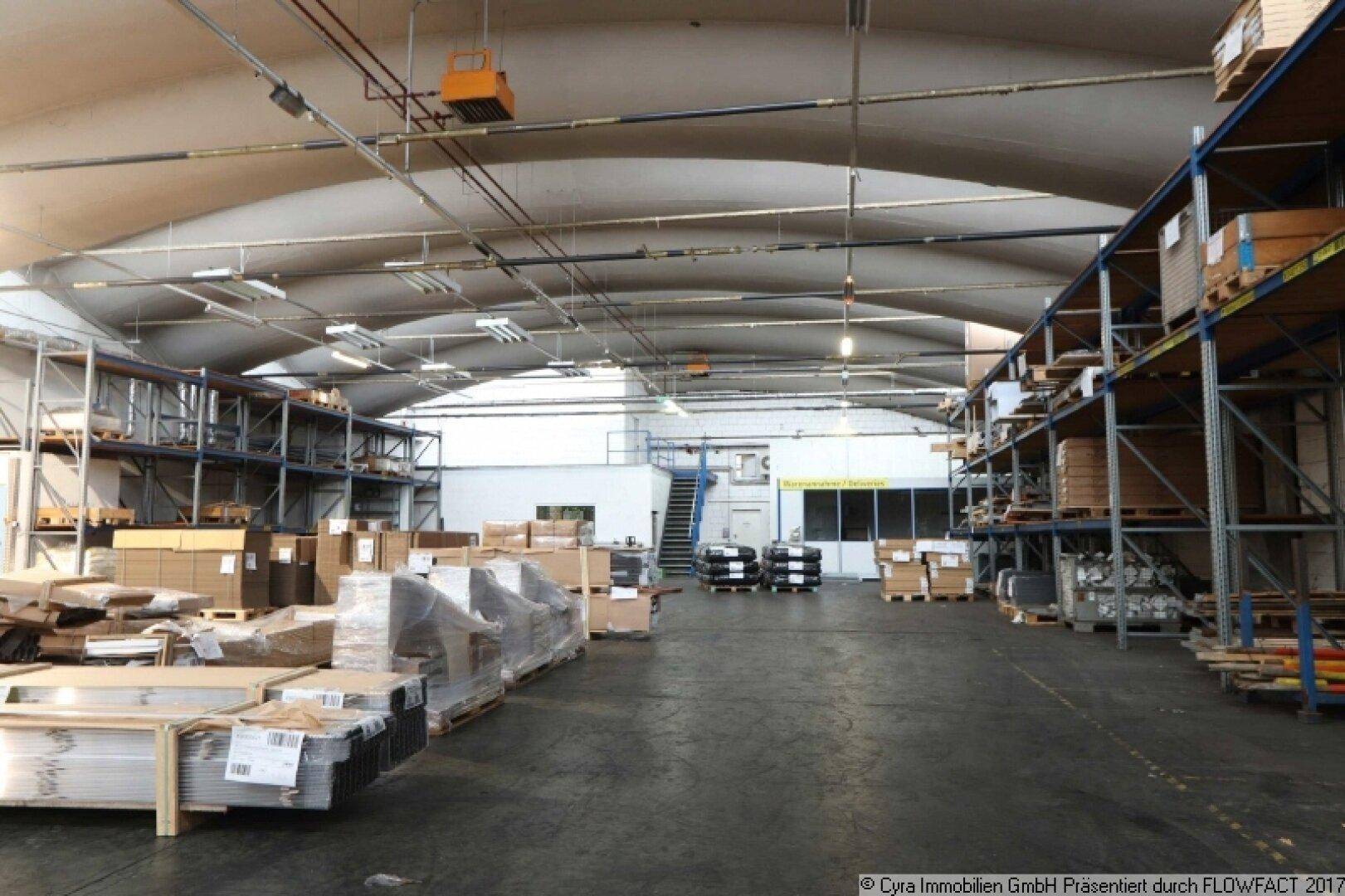 Weitläufige Lagerhalle mit gewölbter Decke, gefüllt mit Waren auf Regalen und einem Zugang zu einer oberen Ebene.