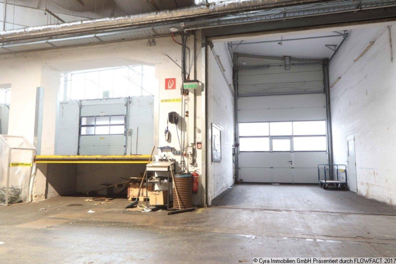 Ladebereich einer Industriehalle mit zwei großen Rolltoren und einer erhöhten Laderampe für effiziente Logistik.