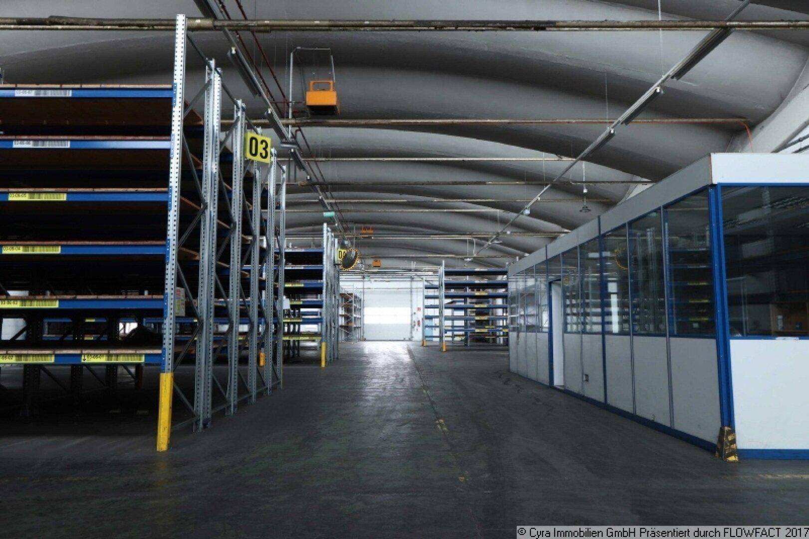 Lagerhalle mit hohen Regalen und einer abgetrennten Büroeinheit, die eine funktionale Arbeitsumgebung bietet.