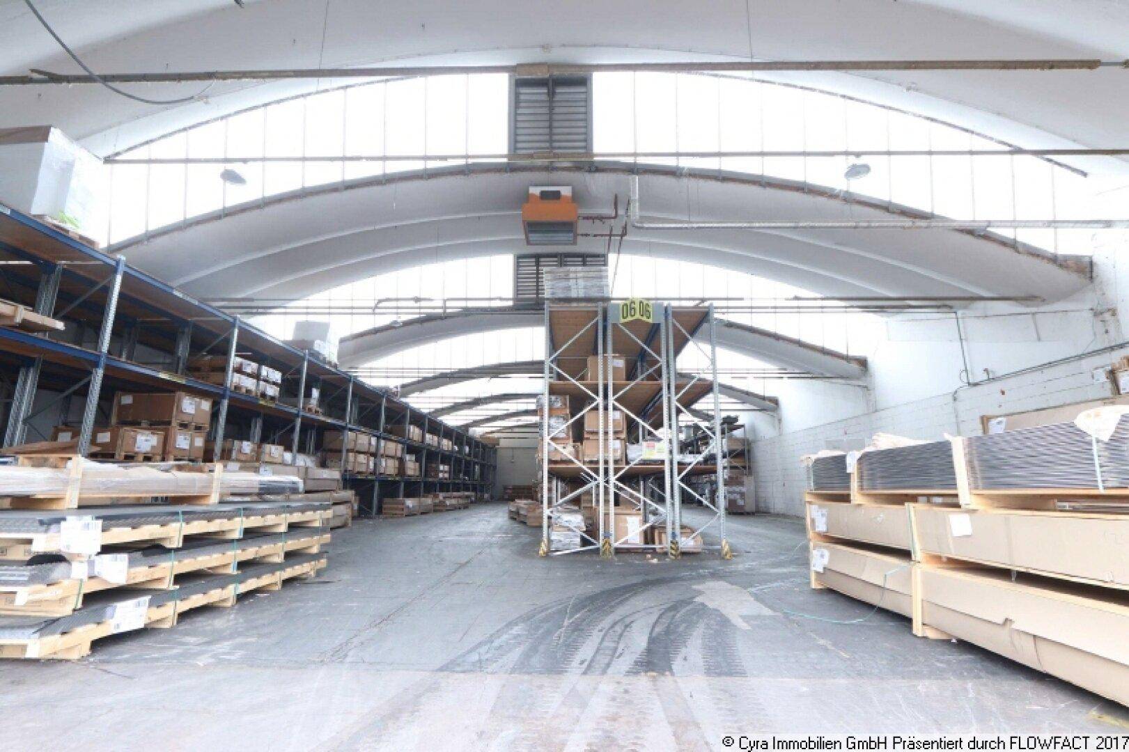 Lagerhalle mit gestapelten Waren auf Paletten und hohen Regalen, bereit für den Versand oder die weitere Verarbeitung.
