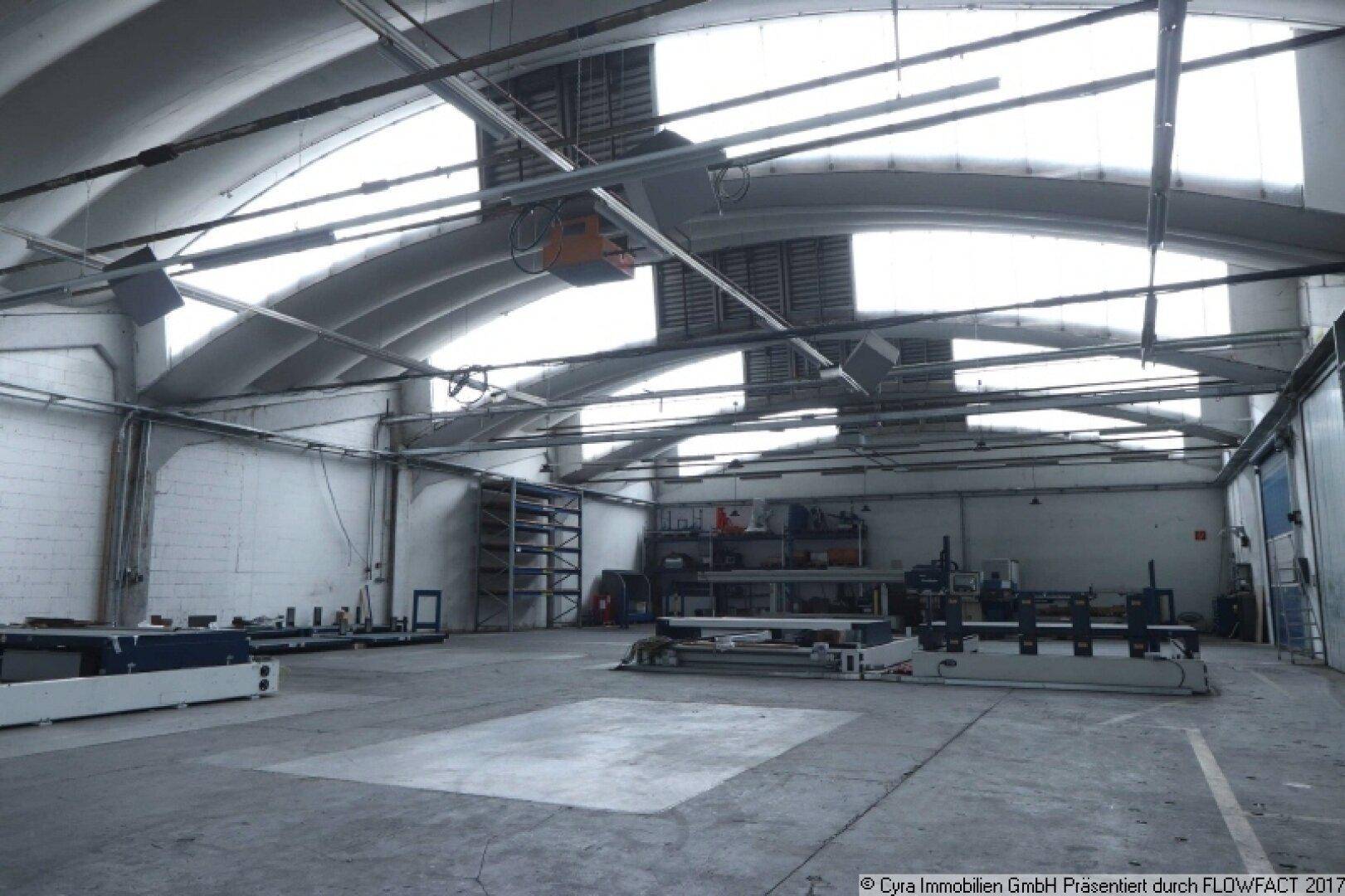 Werkstattbereich in einer Industriehalle mit Arbeitsflächen, Regalen und viel Tageslicht durch die Fenster.