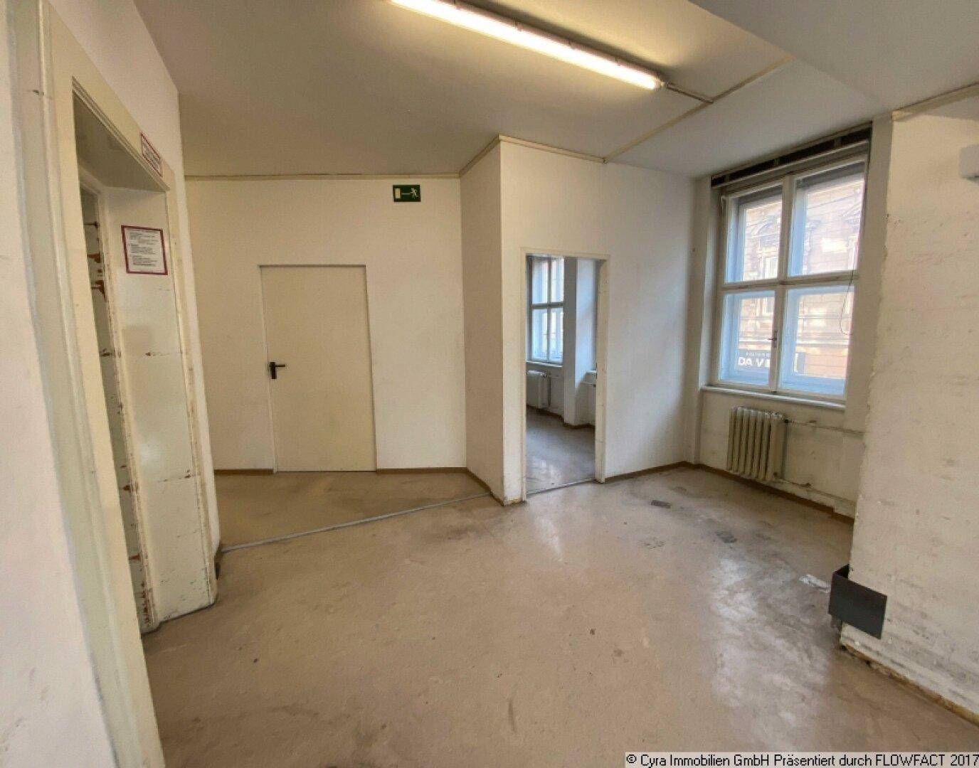 Innenraum mit mehreren Türen, großen Fenstern und einem abgenutzten Boden, der Renovierung erfordert.
