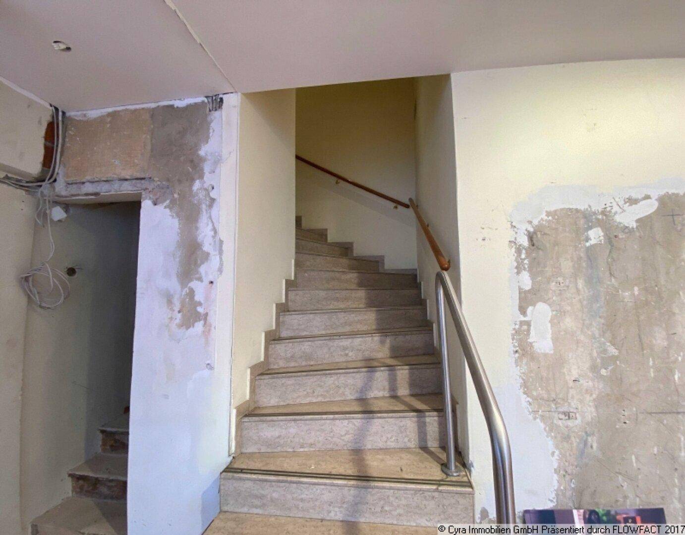 Steintreppe mit Metallgeländer und Holzhandlauf, die in einem renovierungsbedürftigen Zustand ist.