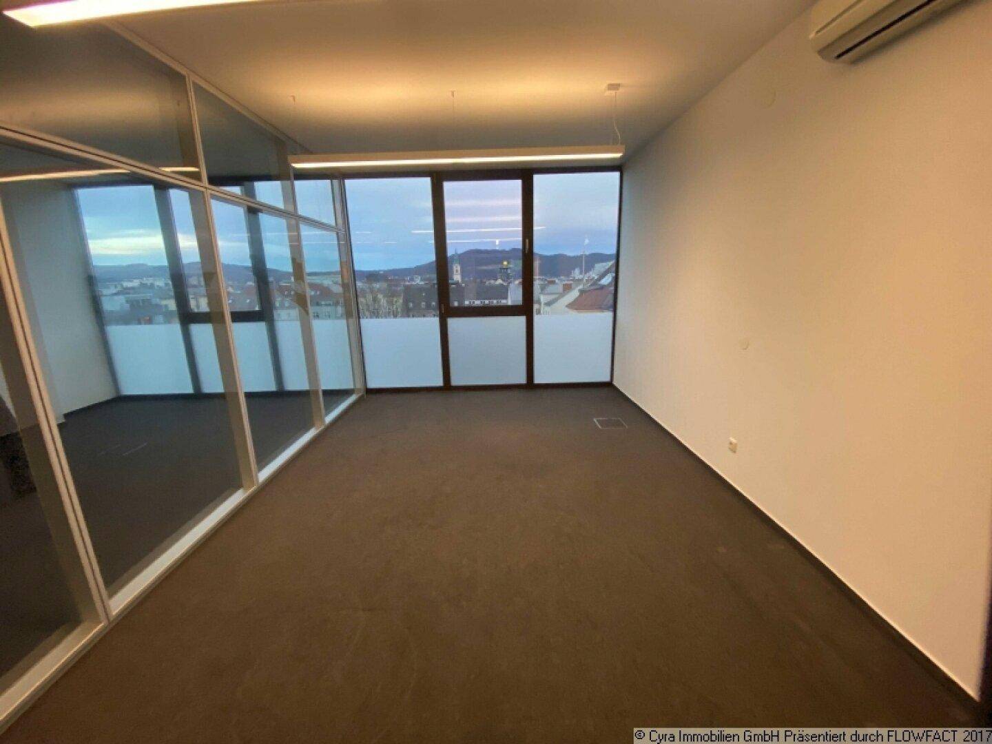 Heller Büroraum mit großen Fenstern, die einen weiten Blick über die Stadt bieten, und Teppichboden.