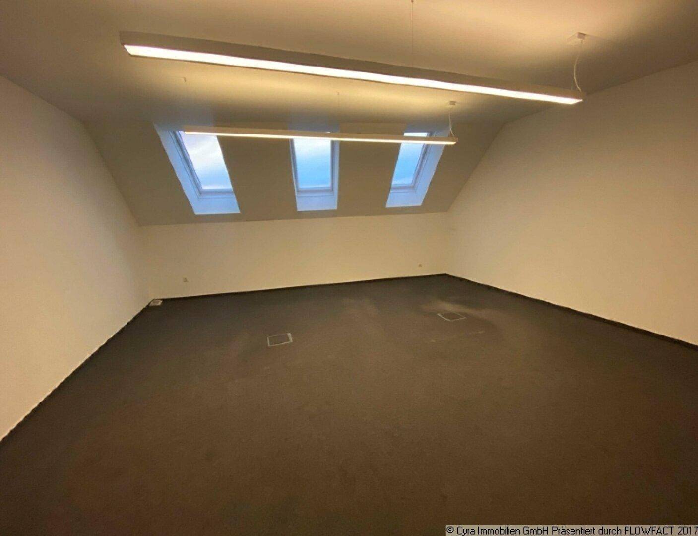 Heller Büroraum im Dachgeschoss mit Teppichboden und mehreren Dachfenstern für Tageslicht.