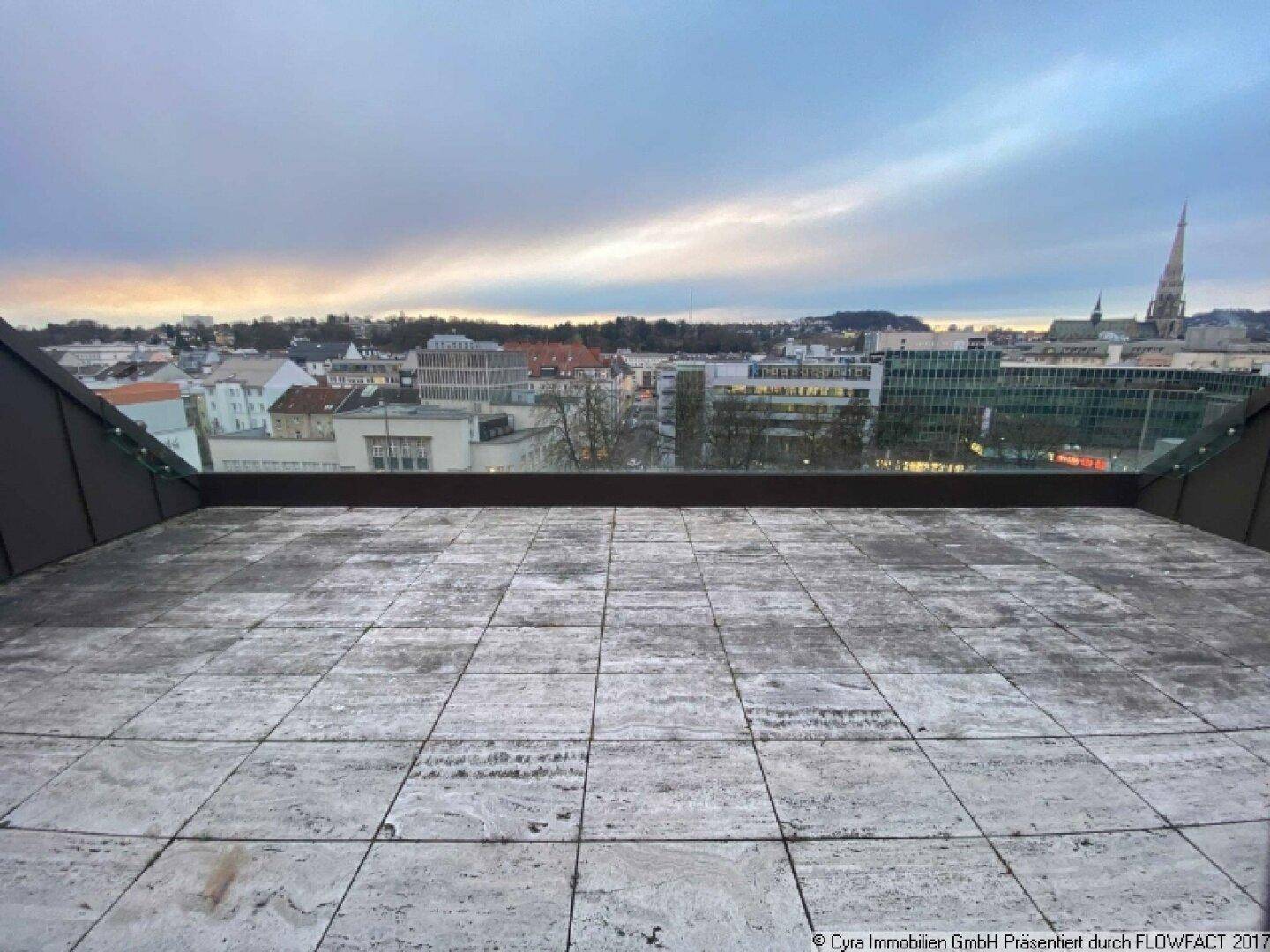 Weitläufige Dachterrasse mit Fliesenboden und Panoramablick auf die Stadt und den Horizont.