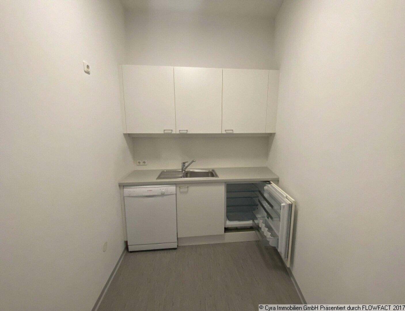 Kompakte Einbauküche mit weißen Oberschränken, Spüle, Geschirrspüler und integriertem Kühlschrank.