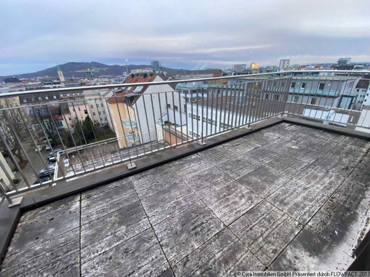 Geräumige Dachterrasse mit Metallgeländer und Blick auf die städtische Umgebung und Berge.
