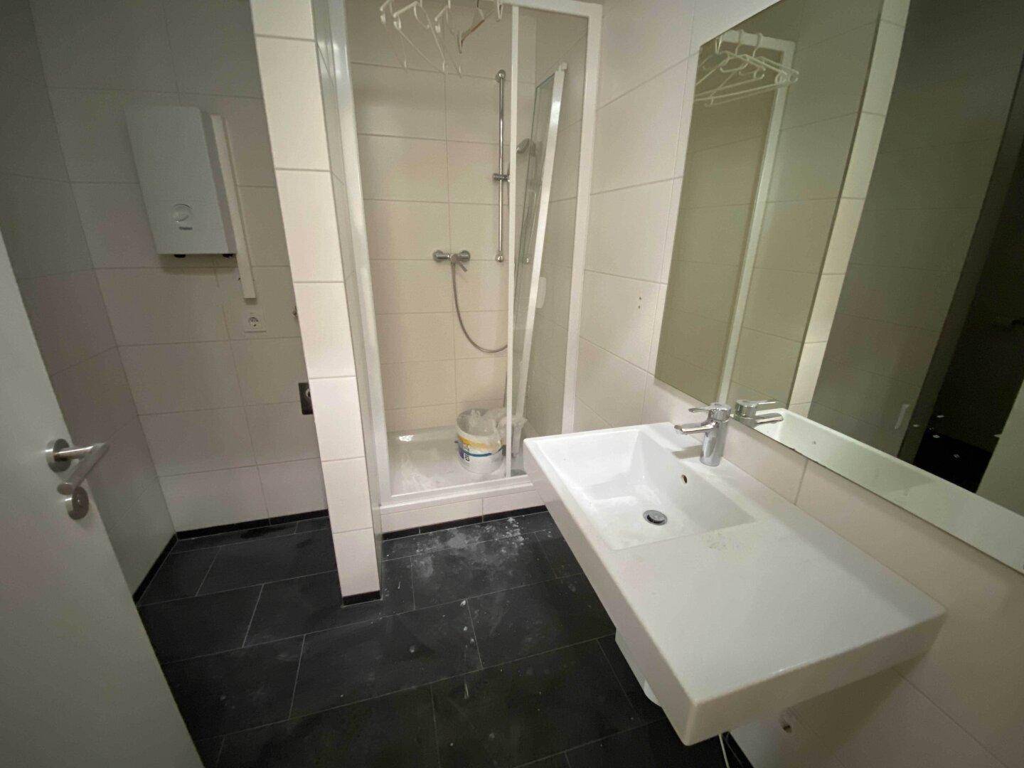 Modernes Badezimmer mit Duschkabine, weißem Waschbecken und dunklen Fliesen am Boden.