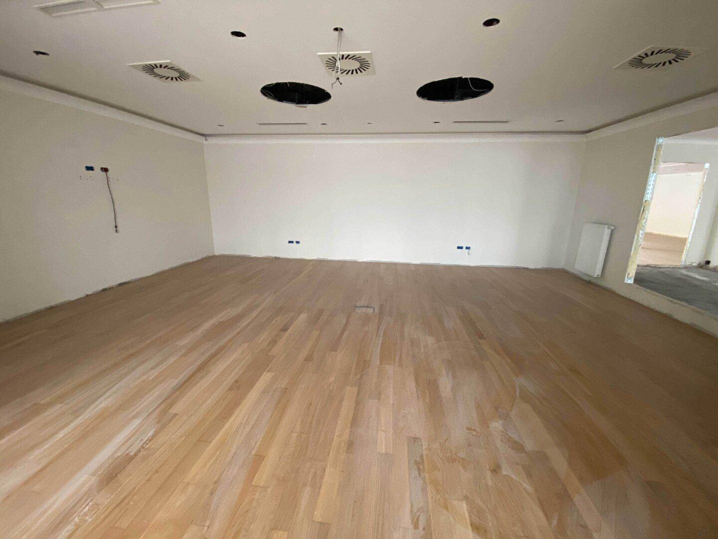 Heller, weitläufiger Raum mit neu verlegtem Holzparkett und abgehängter Decke, bereit zur Fertigstellung.