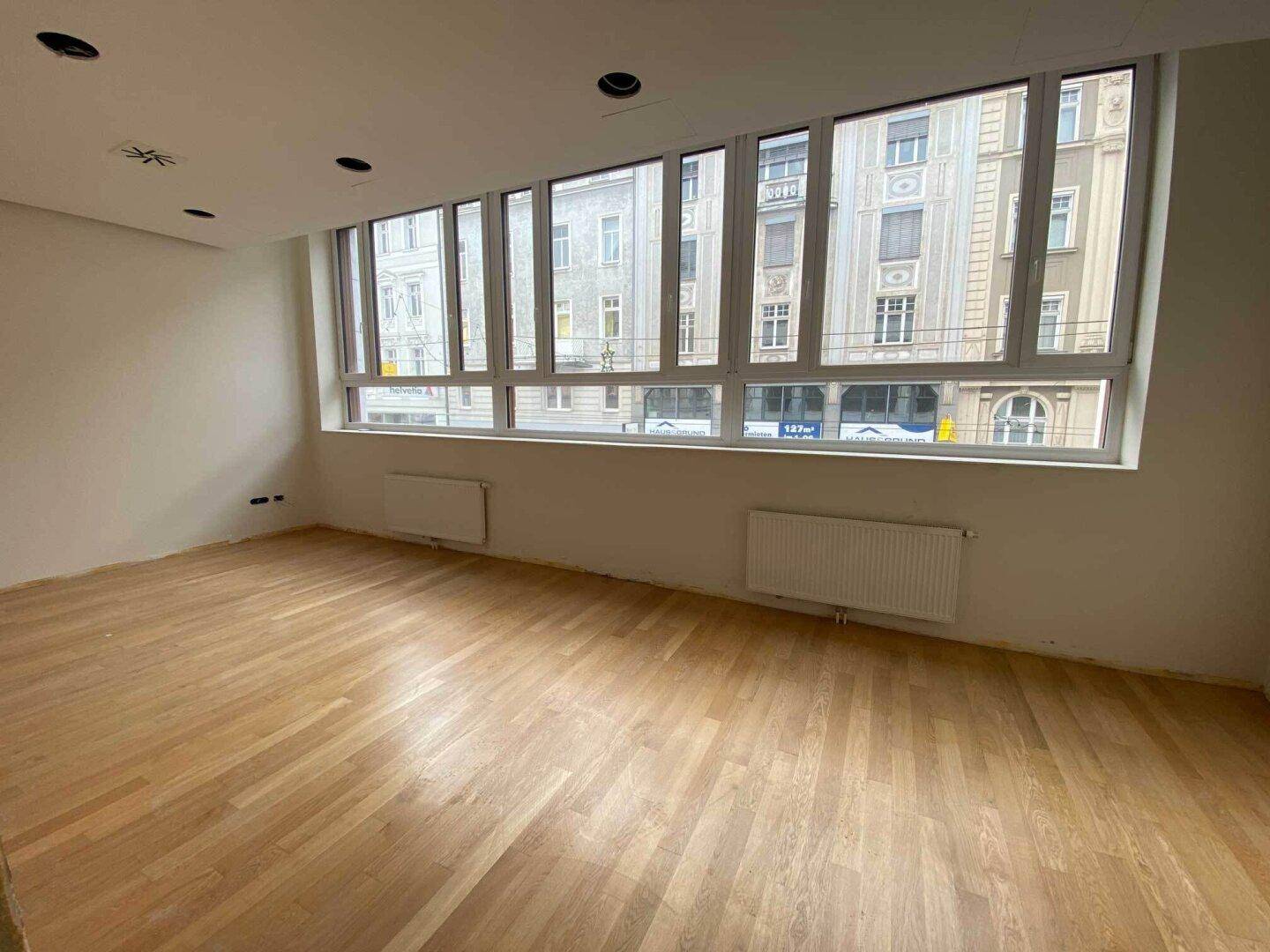 Heller, offener Raum mit Holzparkett und einer Fensterfront mit Blick auf die Stadt.