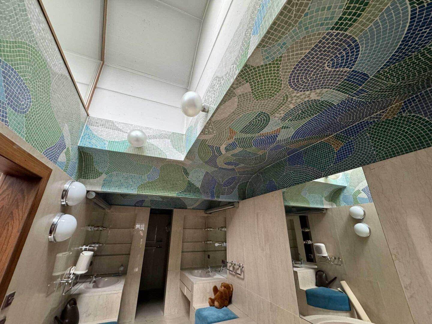 Einzigartiges Badezimmer mit farbenfrohen Mosaikfliesen an Decke und Wänden sowie Oberlichtern.