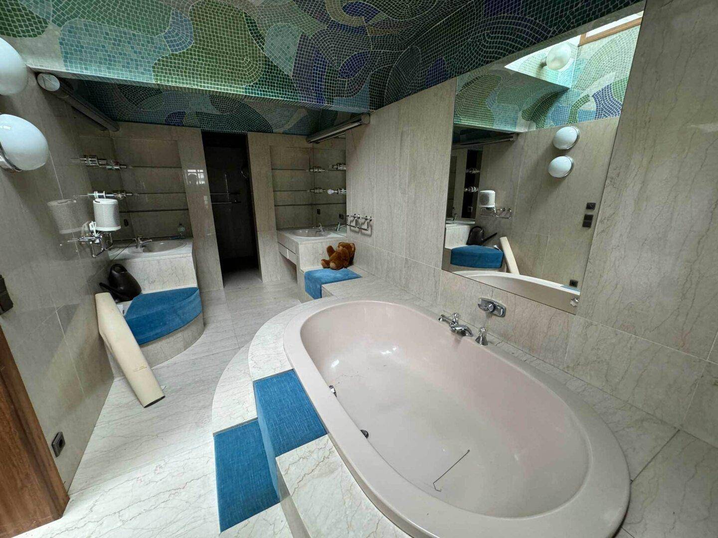 Geräumiges Badezimmer mit großer Badewanne, Marmorfliesen und dekorativen Mosaikdecken.