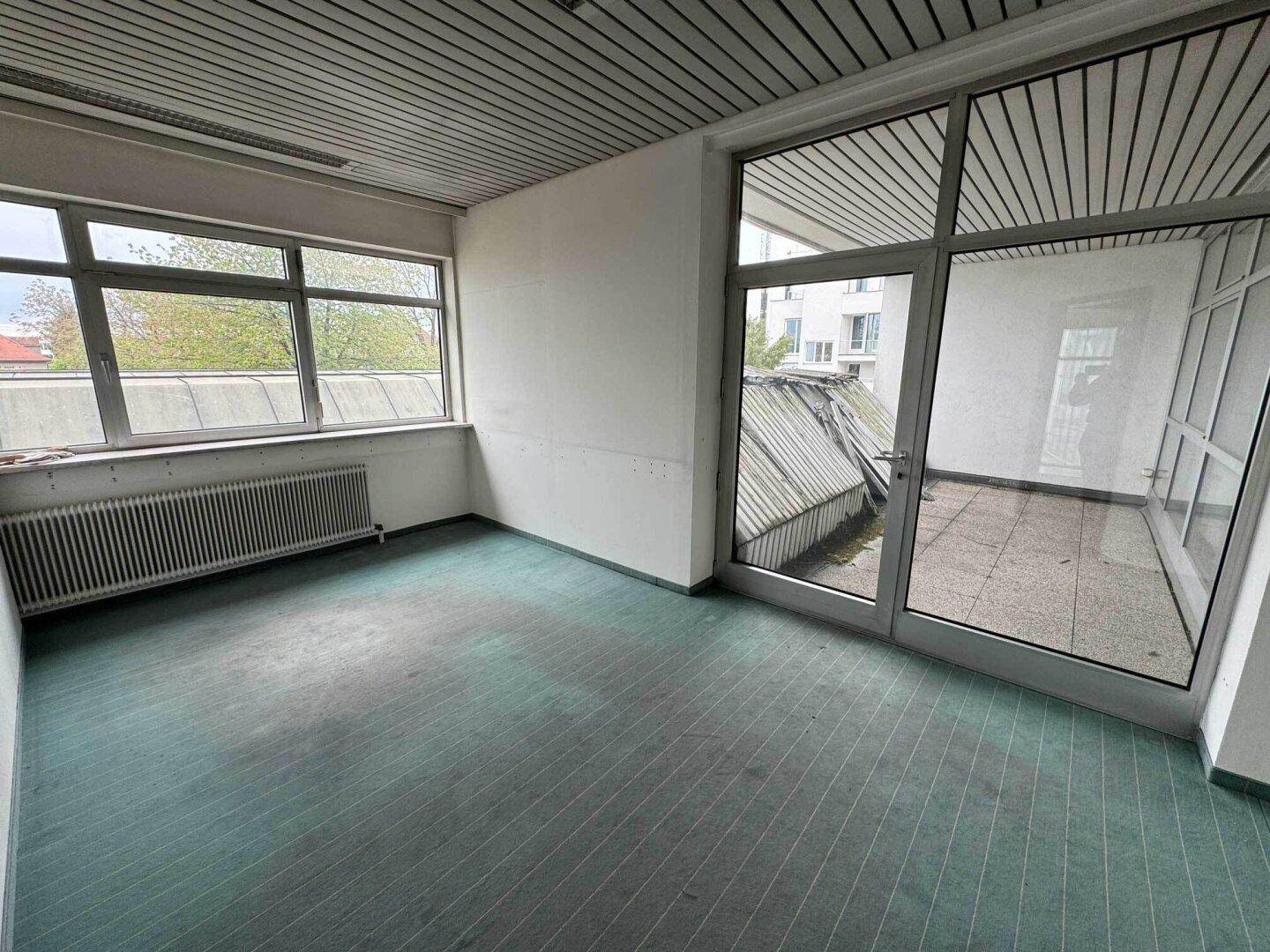 Raum mit grünem Teppichboden und Zugang zu einem verglasten Balkon oder einer Loggia.