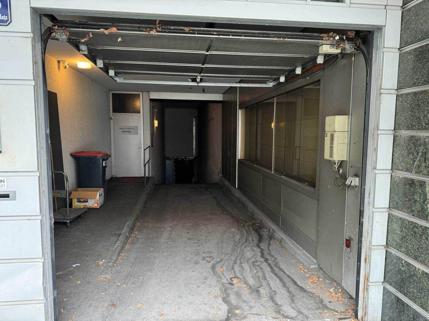 Eingangsbereich einer Garage oder Laderampe mit offenem Rolltor und Betonboden.