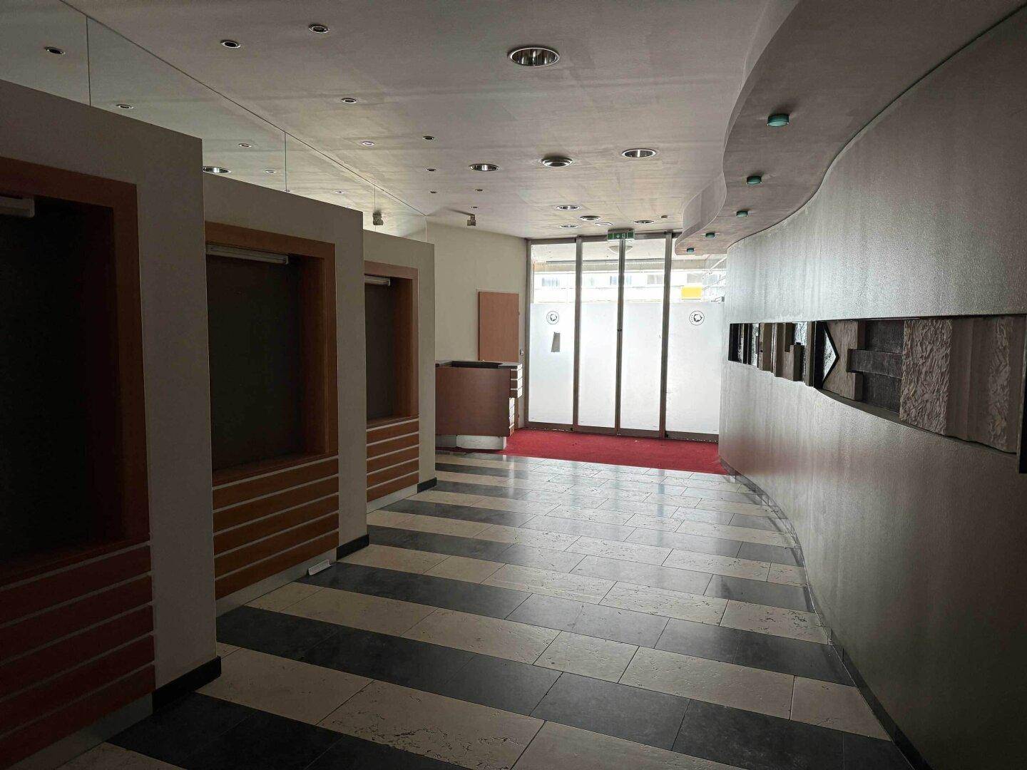 Langer Flur oder Lobby mit gestreiftem Fliesenboden und Glasfront zum Eingangsbereich.