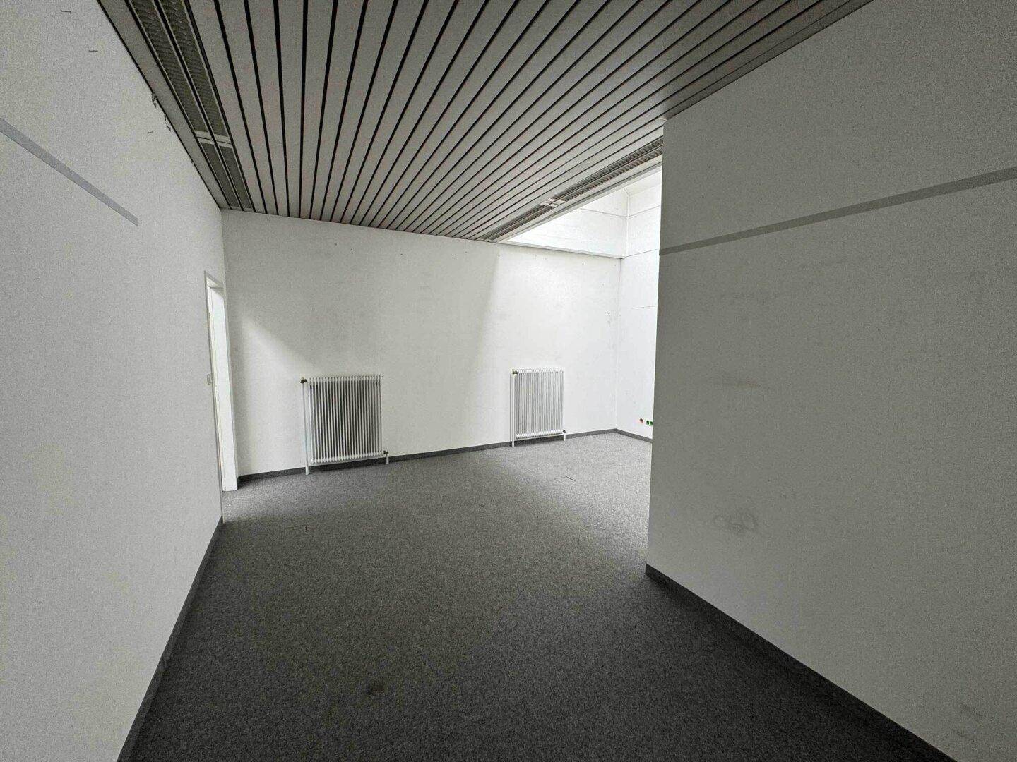 Büroraum mit grauem Teppichboden und Heizkörpern an den Wänden, bereit zur Einrichtung.