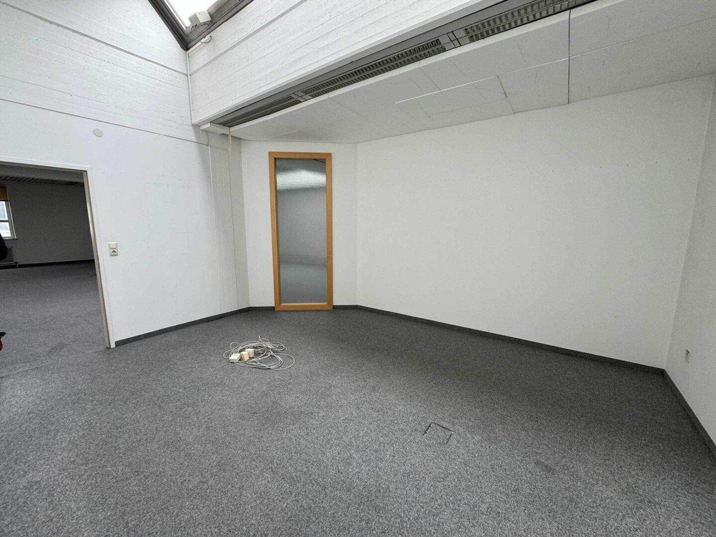 Heller Raum mit Teppichboden, weißen Wänden und schrägen Deckenfenstern, ideal als Büro.