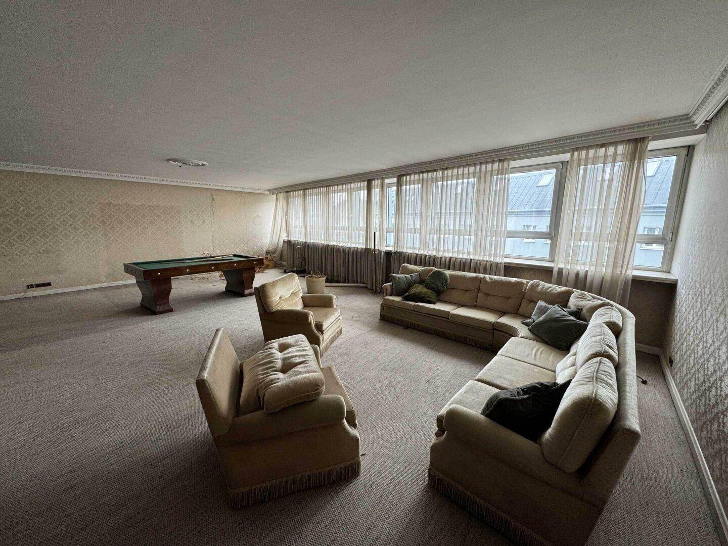 Geräumiges Wohnzimmer mit Teppichboden, gemusterter Tapete und Billardtisch, mit großen Fenstern.