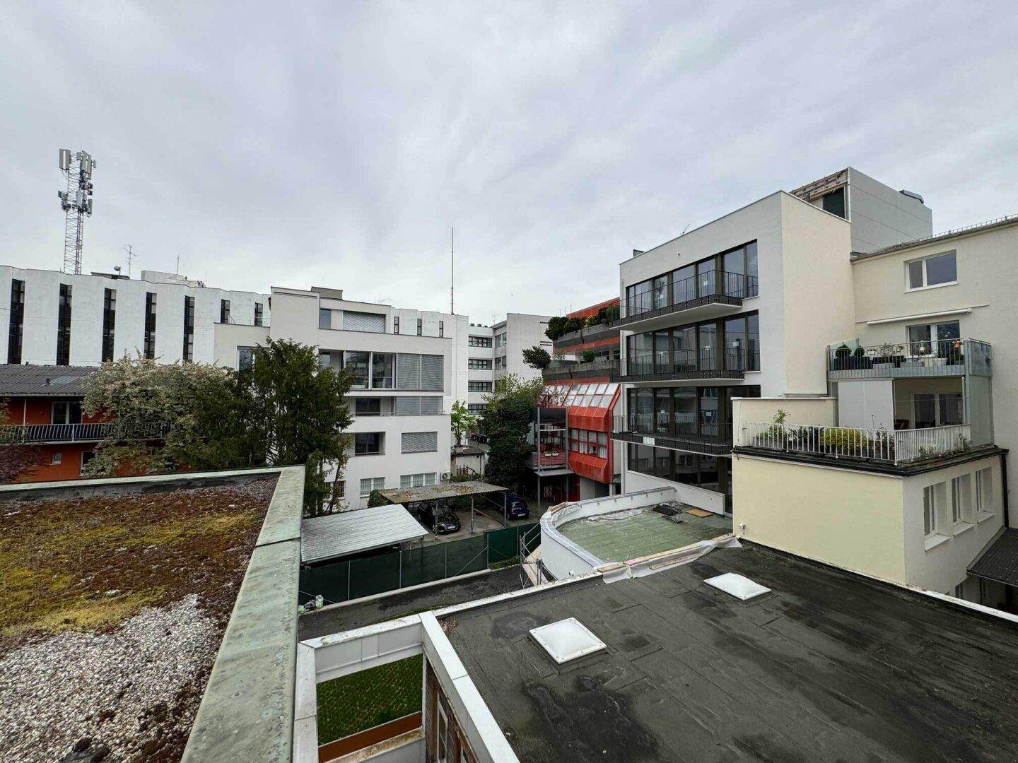 Blick von einem Dach auf umliegende moderne Gebäude und eine städtische Umgebung unter bewölktem Himmel.