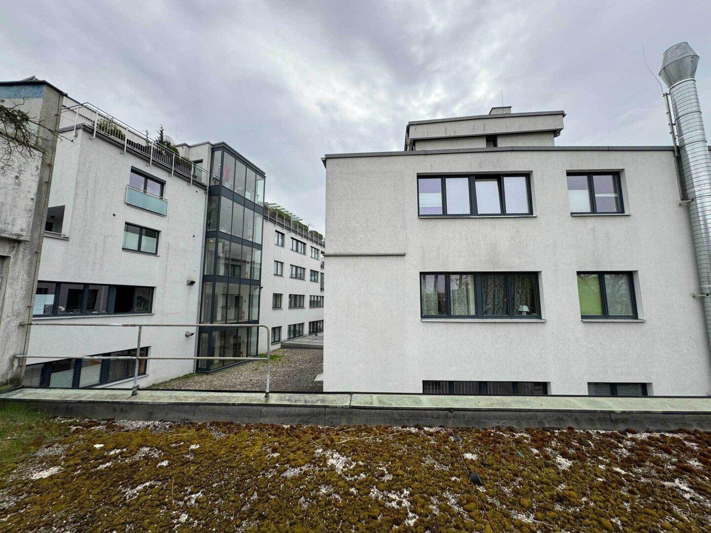 Außenansicht von zwei modernen Gebäuden mit großen Fenstern und einem gläsernen Aufzugsschacht.