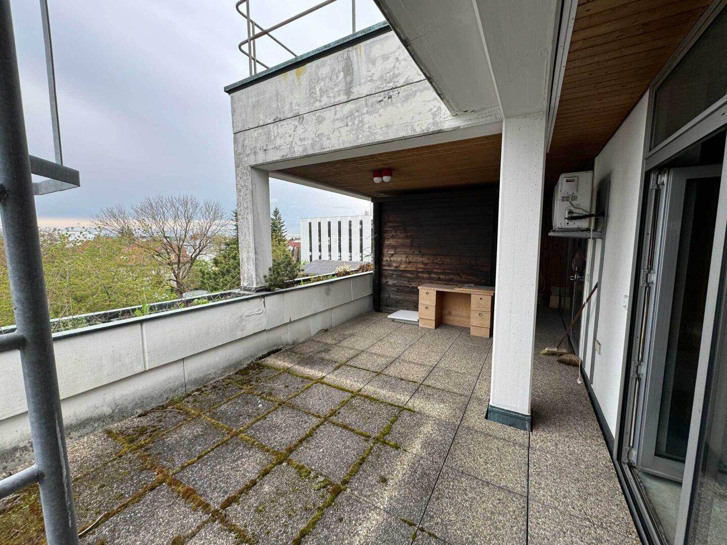Überdachte Terrasse mit Fliesenboden und Blick ins Grüne.