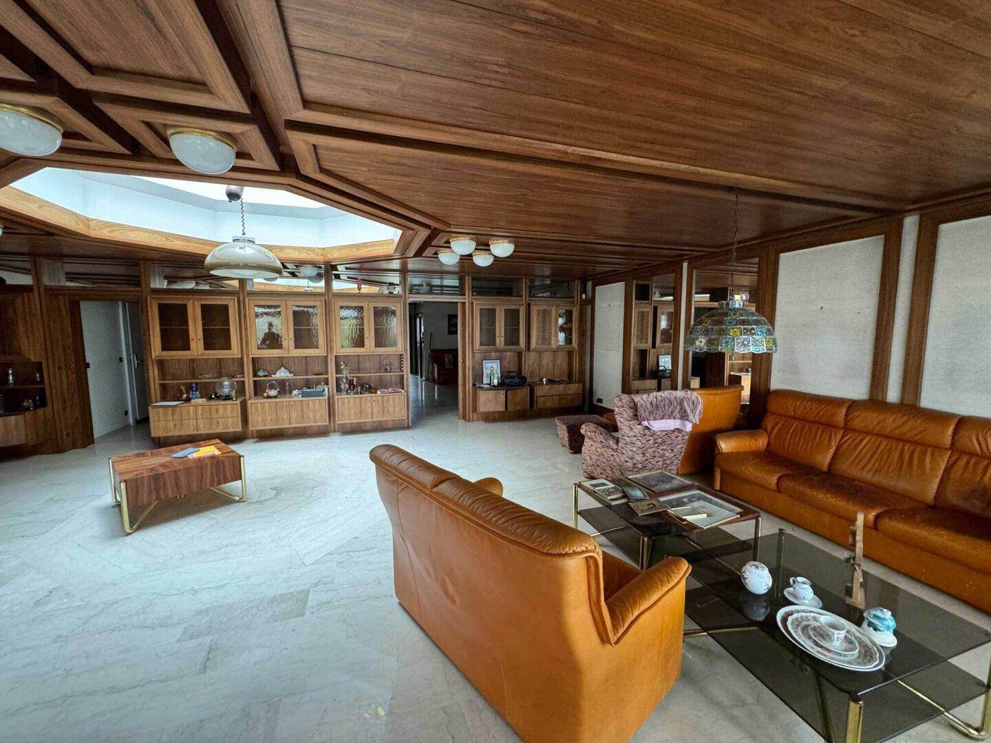 Großzügiges Wohnzimmer mit Marmorboden, Holzdecken und Einbauschränken.