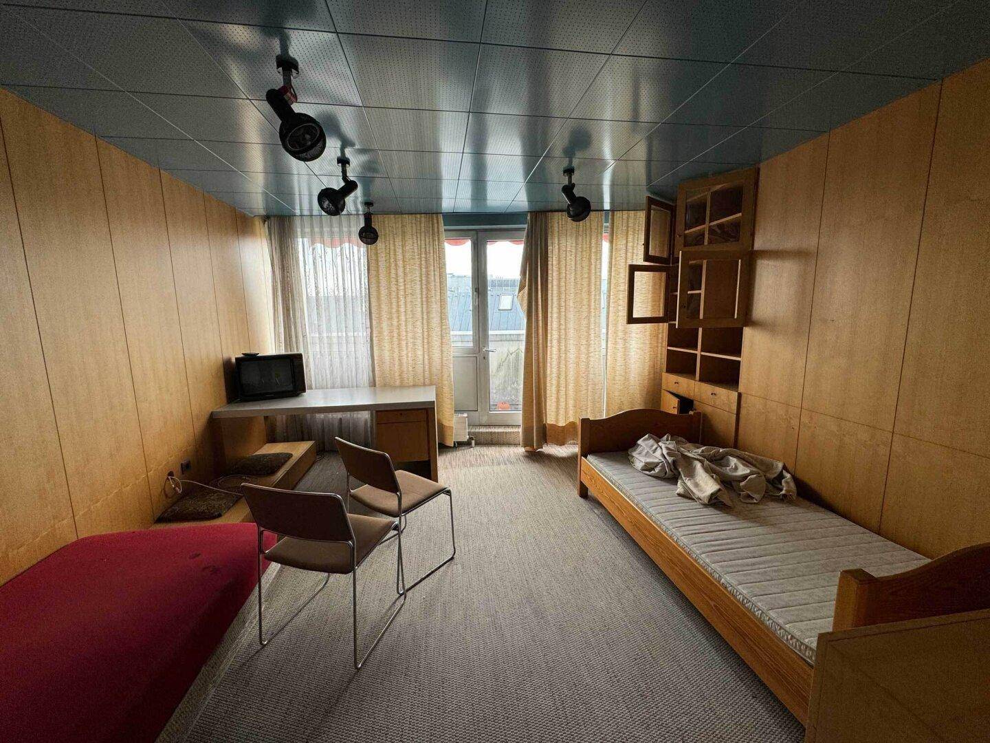 Schlafzimmer mit Einzelbett, Schreibtisch und Holzvertäfelung an den Wänden.