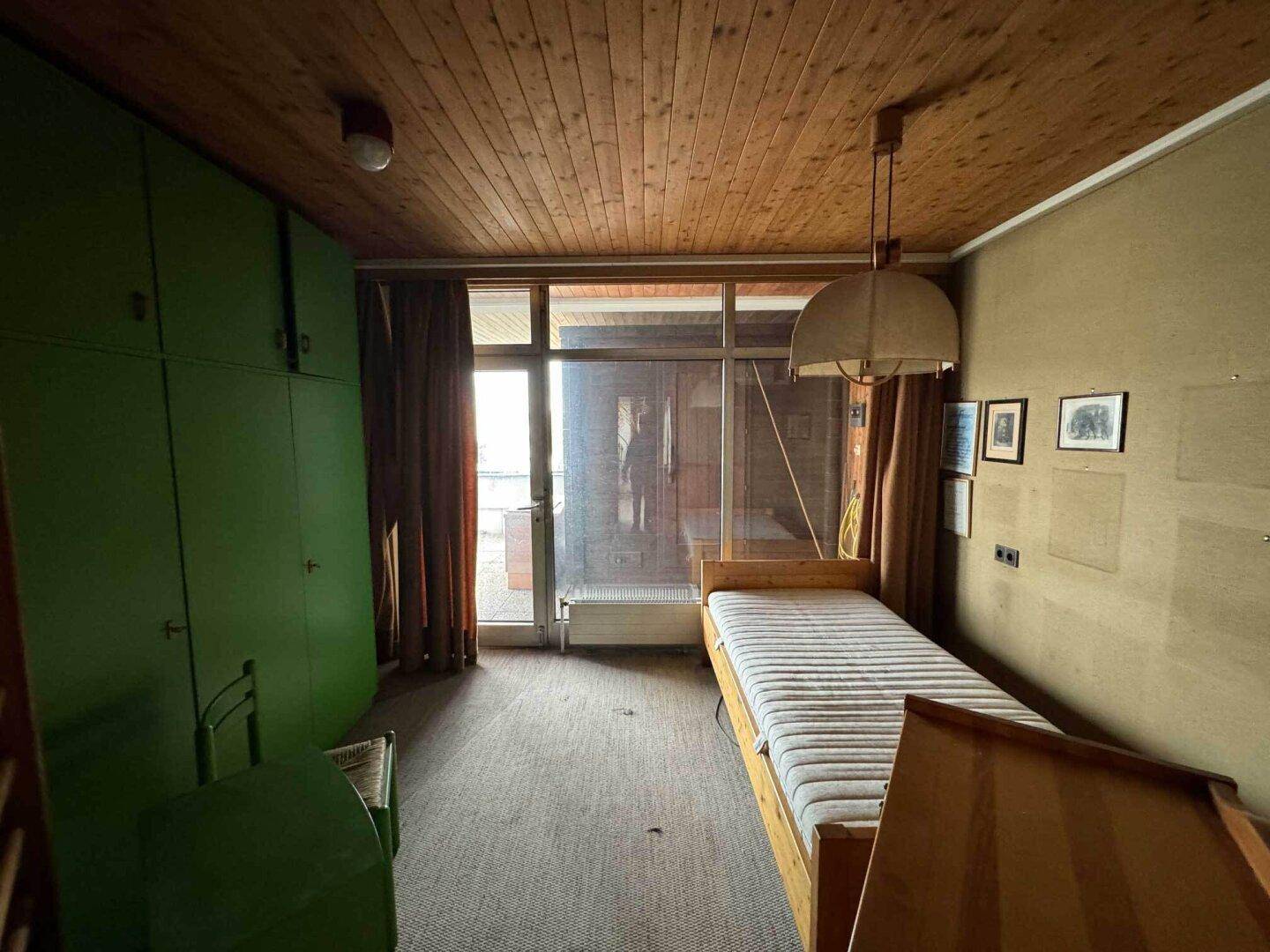 Schlafzimmer mit Einzelbett, grünen Einbauschränken und Holzdecke.