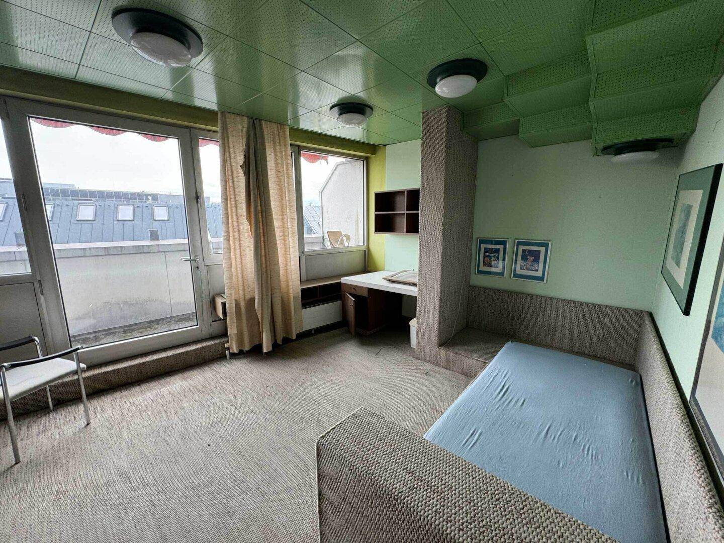 Helles Schlafzimmer mit Einzelbett, Schreibtisch und Zugang zum Balkon.