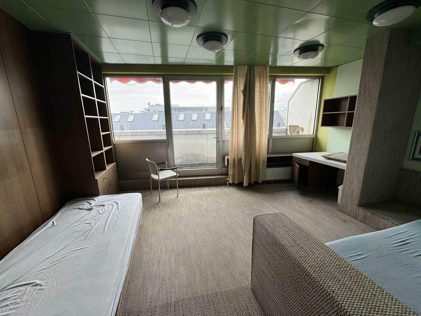Schlafzimmer mit zwei Einzelbetten, Schreibtisch und Zugang zum Balkon.