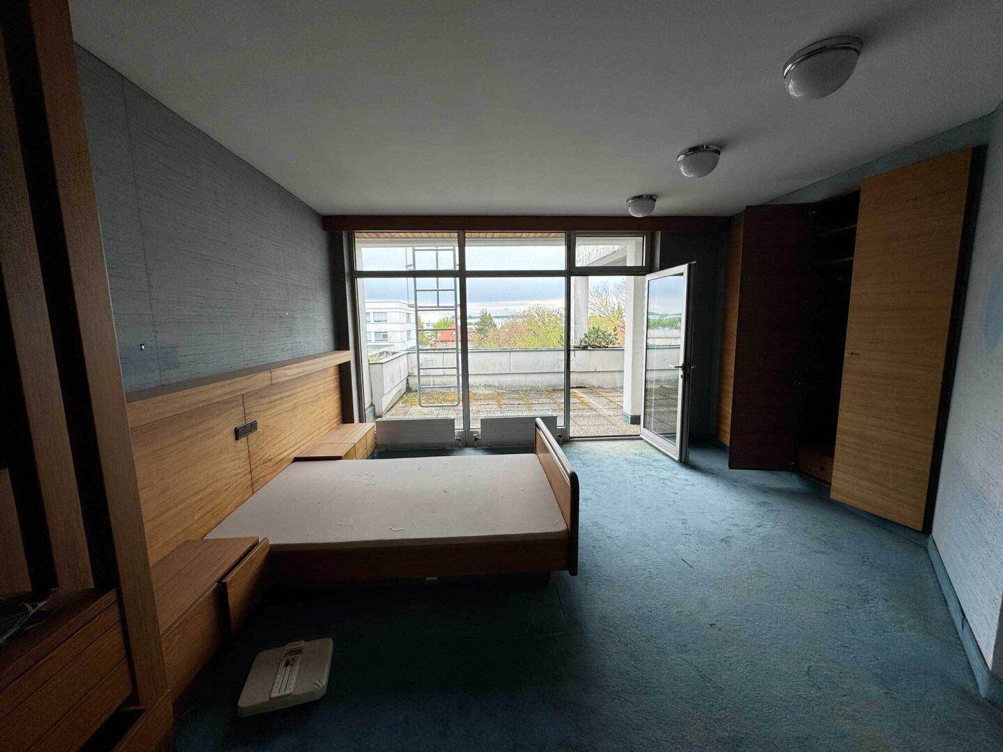 Schlafzimmer mit blauem Teppichboden, Einbauschränken und Zugang zu einem Außenbereich.