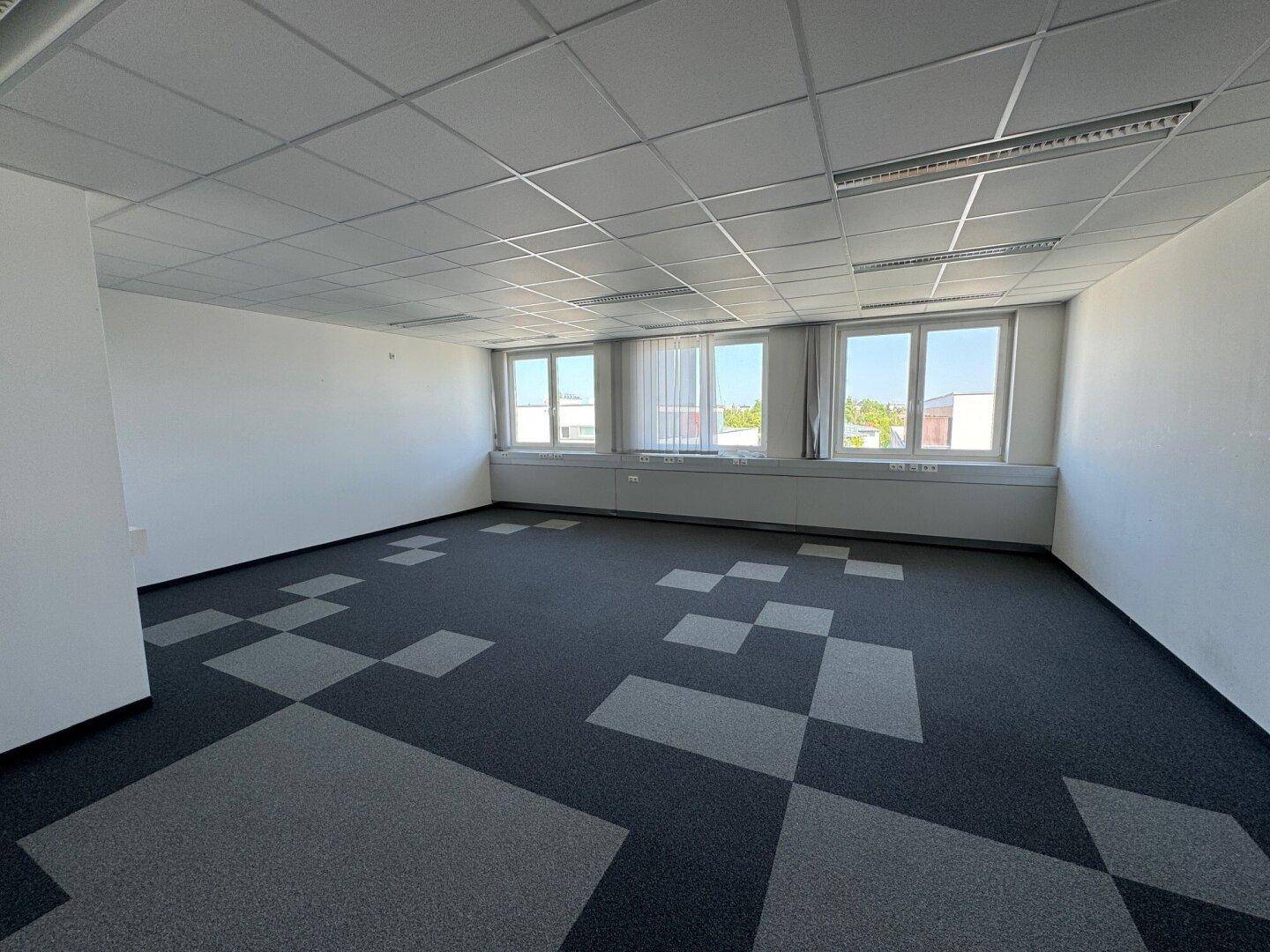 Heller Büroraum mit Teppichboden in Grau- und Schwarztönen und großen Fenstern für viel Tageslicht.