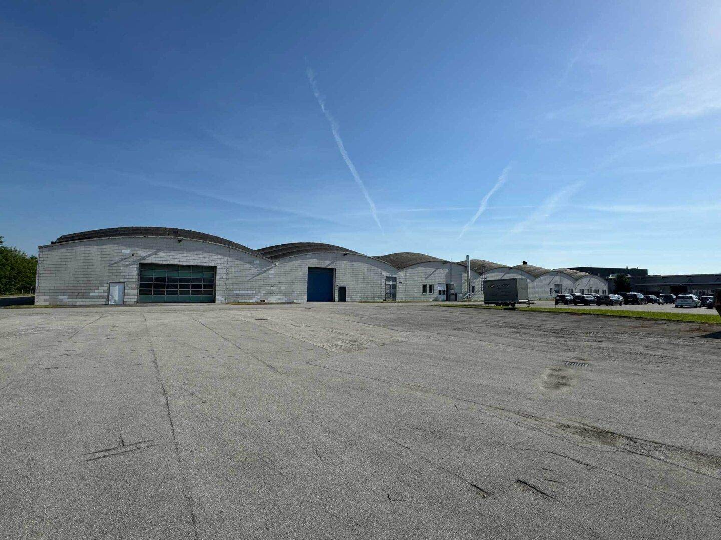 Panoramablick auf mehrere Industriehallen mit markanten Runddächern und einer weitläufigen Freifläche für Fahrzeuge an einem sonnigen Tag.