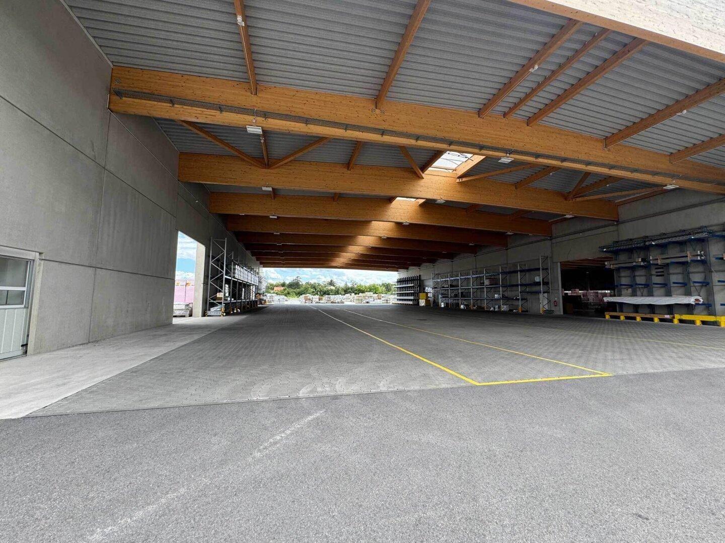 Überdachte Ladezone einer Lagerhalle mit Holzbalkenkonstruktion, Betonboden und natürlichem Lichteinfall.